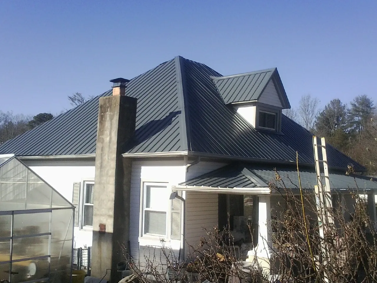 Dark blue standing seam metal roof on a white farmhouse with dormer — Slate & Tile Roof Repair by Roofing Brothers in Hensonville