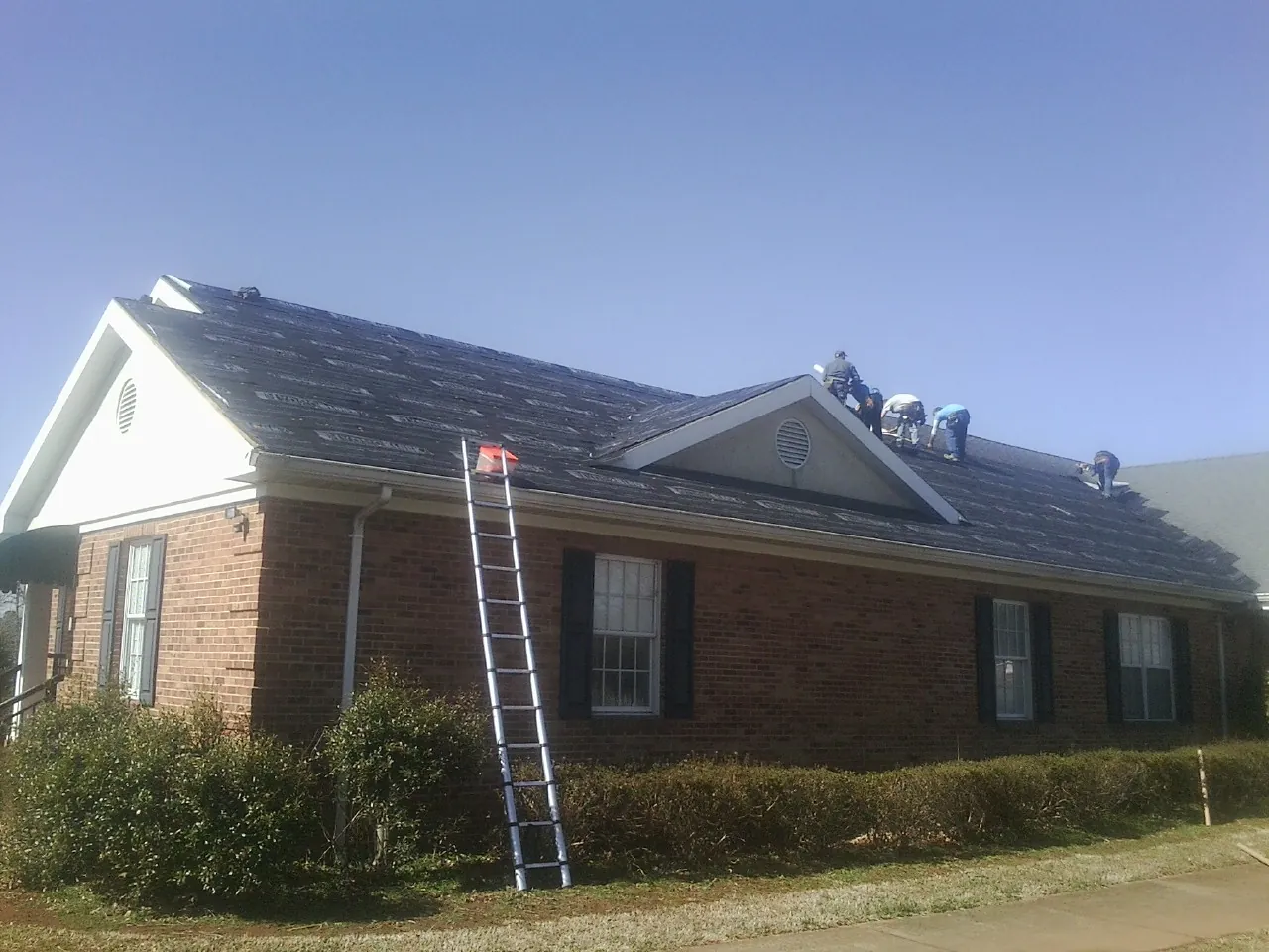 Crew tearing shingles off a brick ranch roof with a ladder set — Metal Roof Repair work by our crew in Hensonville