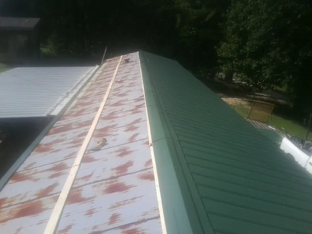 Old rusted panels beside newly installed green metal roofing — Wind Damage Roof Repair by Roofing Brothers in Hensonville