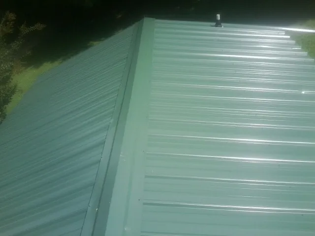 New green metal panels meeting at the ridge of a roof — Flat Roof Repair work by our crew in Hensonville