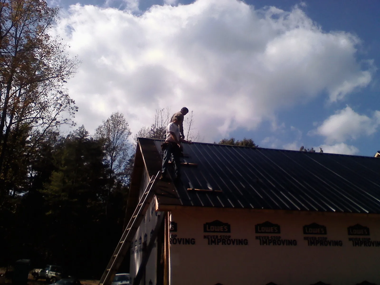 Roofer fastening dark metal panels high against a cloudy sky, from a Roof Inspection job in Hensonville