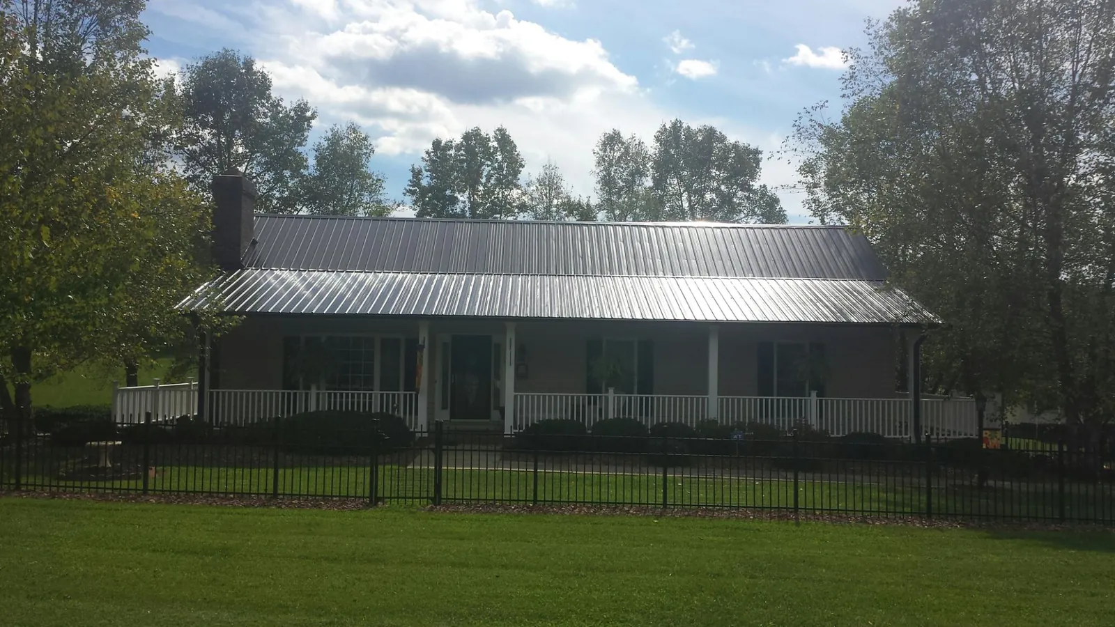Gray metal roof on a brick ranch with a full width front porch — Gutter Guard Installation work by our crew in Hensonville