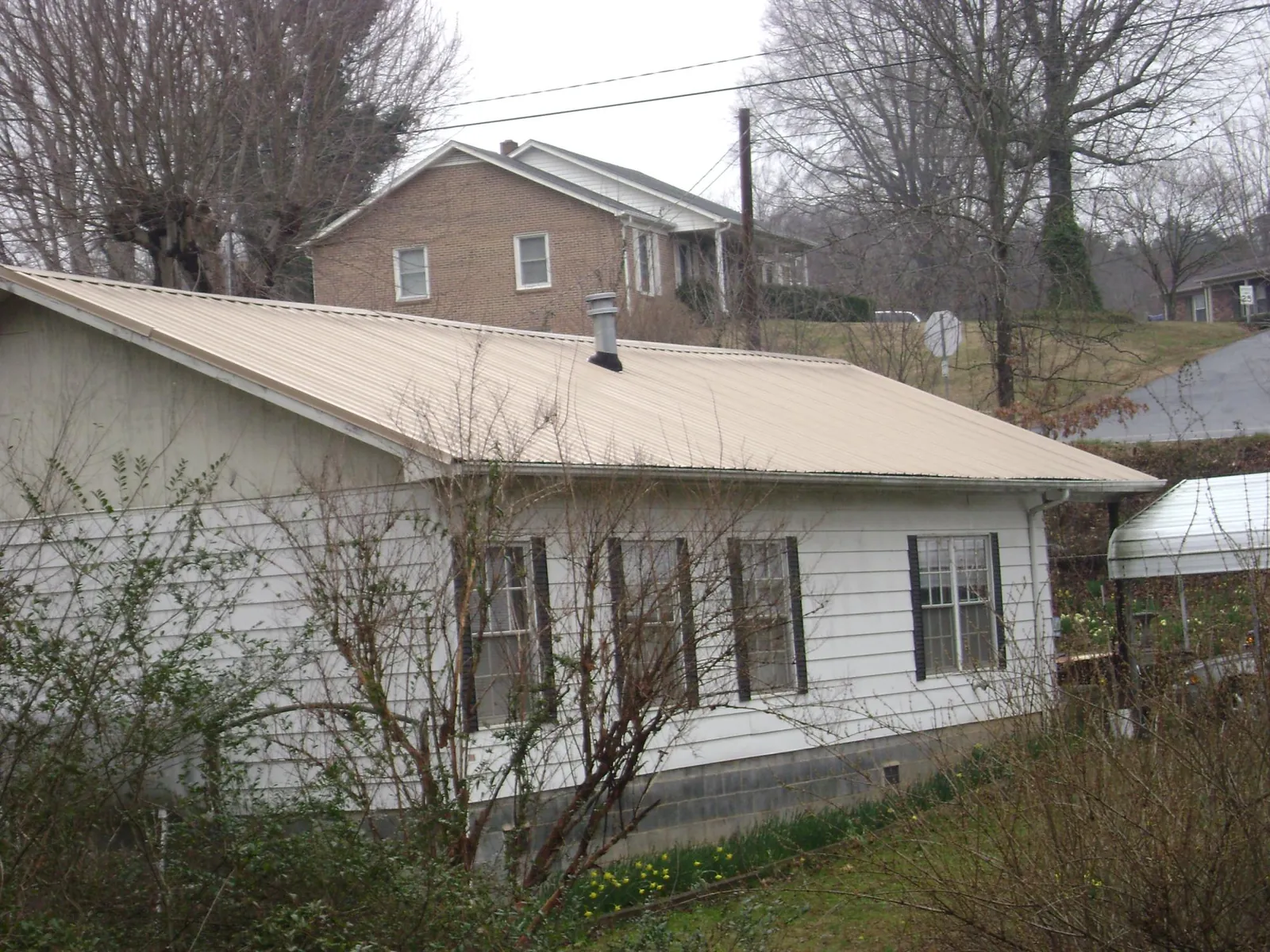 Tan metal roof on a white sided house set into a hillside — Commercial Roofing by Roofing Brothers in Hensonville